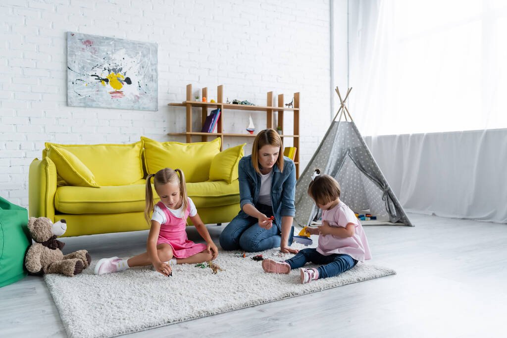 teacher sitting on carpet and playing with toddler girl